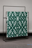 Green fabric with white floral pattern on a black metal frame against a gray wall.