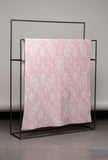 Pink blanket with white floral pattern draped over a black metal rack against a gray wall.