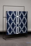 Navy blue blanket with white geometric patterns draped over a black metal frame against a gray background.