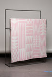 Pink and white patterned blanket on a black metal rack against a gray wall.