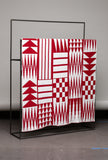 Red and white patterned blanket on a black metal stand against a gray background