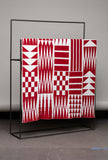 Red and white patterned blanket on a black metal stand against a gray background
