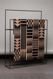 Patterned blanket on a black metal rack against a gray wall.