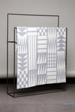 Textile with geometric pattern draped over a black metal frame against a gray background