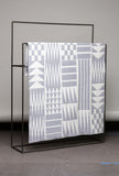 Textile with geometric pattern draped over a black metal frame against a gray background