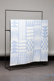 Quilt with geometric pattern on a black metal stand against a gray wall.