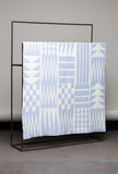 Textile with geometric pattern draped over a black metal rack against a gray wall.