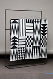 Black and white patterned blanket on a metal stand against a gray background