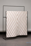 Beige and white patterned blanket on a black metal stand against a gray background