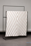Patterned blanket on a black metal rack against a gray wall.