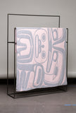 Textile with abstract patterns draped over a black metal frame against a gray background