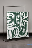 Green and white patterned blanket draped over a black metal stand against a gray background