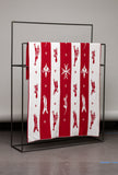 Red and white patterned blanket on a black metal rack against a gray wall.