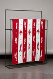 Red and white patterned blanket on a black metal rack against a gray wall.