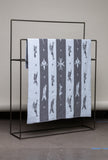 Textile with black and white pattern draped over a black metal rack against a neutral background
