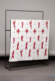 White blanket with red patterns draped over a black metal frame against a gray wall.