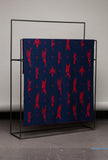 Blue blanket with red geometric pattern on a black metal stand against a gray wall.
