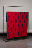Red fabric with black pattern on a metal stand against a plain background