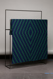 Green and blue patterned blanket on a black metal stand against a gray background