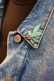 A close-up of a blue denim jacket with a metal leaf-shaped brooch pinned near the collar, worn over a brown top.