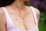 Woman wearing a gold necklace with a heart pendant, blurred green and purple background