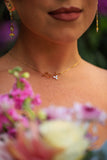 Close-up of a person wearing a gold necklace with a pendant, surrounded by flowers.