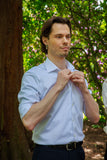 Man adjusting his shirt outdoors with greenery in the background