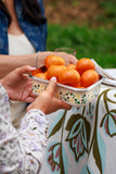 Person holding a container of oranges with a floral-patterned bag in the background