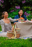Two women enjoying a picnic outdoors with a basket and tablecloth.