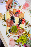 Platter of assorted meats, cheeses, fruits, and crackers on a decorative tablecloth.