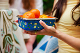 Person holding a blue floral-patterned bowl filled with tangerines.