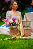 Woman sitting on grass with a picnic basket and flowers