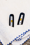 Pair of earrings on a textured white surface with blue trim.