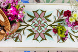 Decorative table runner with floral patterns and flowers on a table.