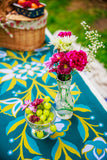 Floral arrangement in a clear vase on a tablecloth with grapes and a basket in the background.