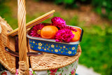 Picnic basket with a floral container holding fruits and flowers on a grassy background