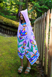Person wrapped in a colorful towel with floral patterns standing outdoors near a wooden fence.