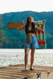 Woman holding a colorful towel and paddle on a wooden dock by a lake.