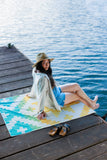 Woman sitting on a colorful towel by the water