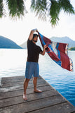 Man holding a colorful towel by a lake with mountains in the background