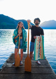Two people on a dock by a lake, holding oars and colorful towels.