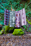 Four geometric patterned wool scarves hanging on a rope line outdoors in a green and mossy forest
