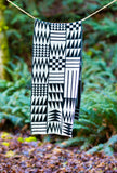 A black and white geometric patterned wool scarf hanging from a rope in an outdoor forest setting