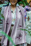A person outdoors wearing a dusty grey geometric patterned knit wool scarf with dark purple geometric stars, standing outdoors in a green forest