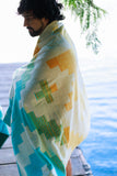 Person wrapped in a patterned towel by a body of water