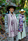 Two people standing outdoors on a forest path, wearing geometric patterned knit wool scarves and wide-brim hats in green woodsy forest