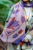 A close-up of a person wearing a geometric patterned knit wool scarf with purple, rust red, and cream maple leafs