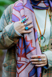 A close-up shot of a person wearing a patterned knit wool scarf with purple, rust red, and cream maple leafs. The person is also wearing multiple rings with turquoise and silver stones.