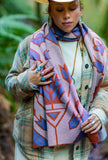 A woman outdoors in a green forest wearing a geometric patterned knit wool scarf with purple, rust red, and cream maple leafs