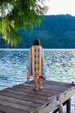 Person standing on a wooden dock by a lake, wearing a colorful striped towel.